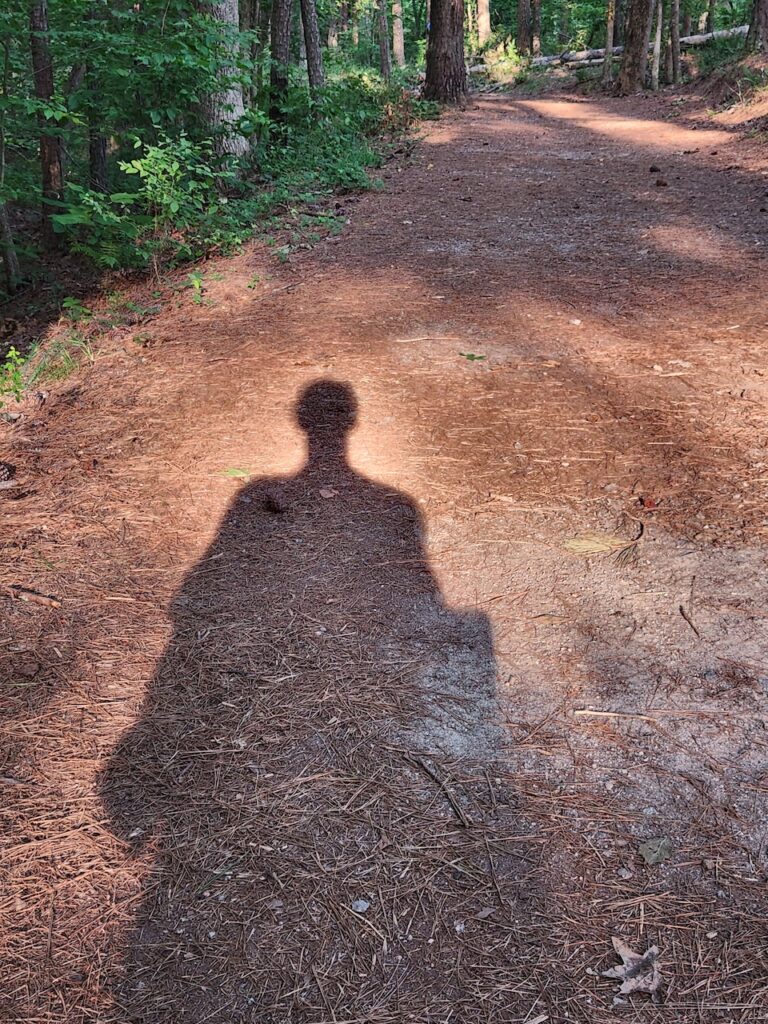 Image Description: The shadow of the author's silhouette upon  a hiking trail. 